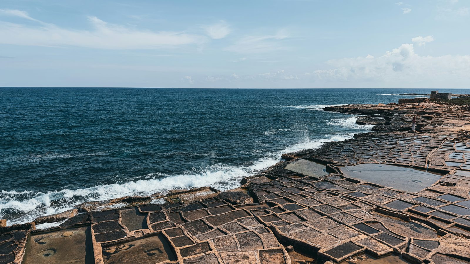 Coastal salt-evaporation pans by the sea, where ambient heat concentrates brine to harvest salt